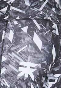 Leggings à motifs noirs et blancs avec des formes géométriques abstraites. Le matériau est extensible, avec une texture lisse et des coutures contrastées.