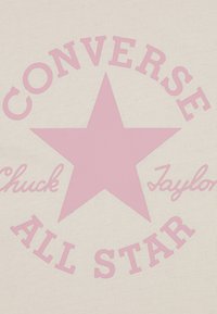 Ljusbeige tyg har en stor rosa stjärna med texten "Converse Chuck Taylor All Star" i en cirkulär uppställning runt den.
