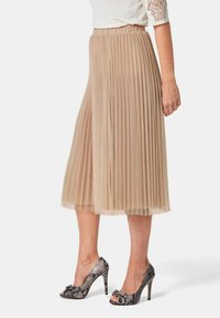 Plissé rok in lichtbeige stof met een elastische tailleband. Gepaard met open teen, hoge hakken met een gestructureerd slangenprint.