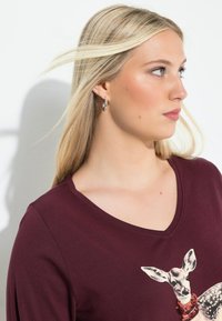 Burgundin värinen V-pääntie T-paita, jossa on hirvisuunnittelu, koristeltu paljeteilla; pehmeää puuvillakangasta; pitkät hihat; sileä pinta.