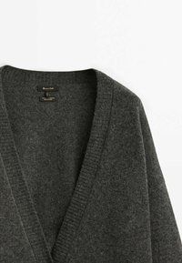 Pull en laine et cachemire gris foncé à col en V avec col en côtes posé à plat sur un fond clair.