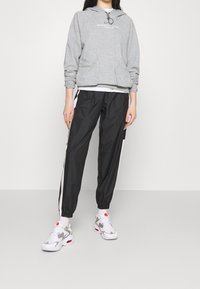 Grå hoodie med framfickor, svarta sportbyxor med vita sidostreck och vita sneakers med grå accenter och röda detaljer.