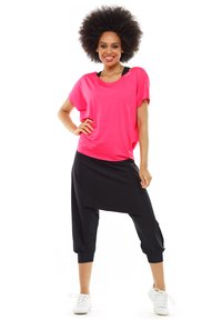 Heldere roze oversized t-shirt gecombineerd met zwarte, loszittende harem pants. Kenmerken zijn een comfortabele pasvorm en elastische manchetten. Witte sneakers maken de look compleet.