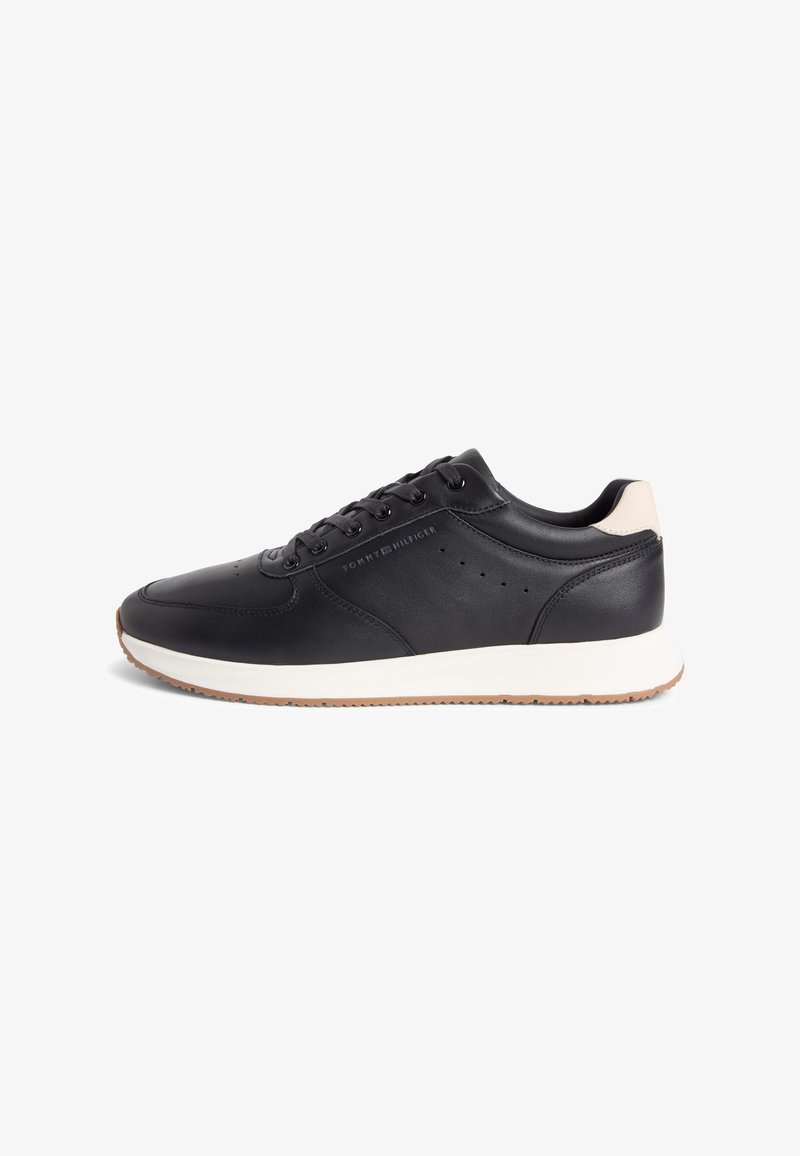 Baskets basses en cuir noir avec semelle blanche, languette de talon beige, lacets noirs et logo "Tommy Hilfiger" sur le côté.