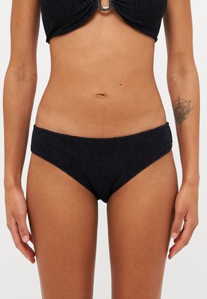 Melna bikini komplekts ar teksturētu augšdaļu un zemu vidukļa apakšdaļu. Audumam ir aušanas raksts, un augšdaļā ir centrālais metāla akcents.