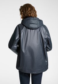 Giacca impermeabile di un blu scuro, con cappuccio, finitura testurizzata e vestibilità ampia. Presenta maniche raglan e un orlo leggermente curvo.