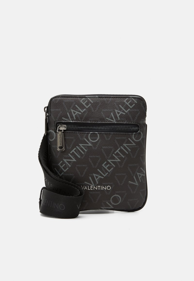 Compact black Valentino crossbody bag with repeating logo pattern, front zip pocket, and adjustable branded shoulder strap.