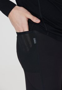 Zwarte sportleggings met een textuur mesh zak aan de rechterkant, voorzien van een klein merklabel. Glad materiaal met een aansluitend ontwerp.