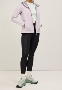 Ljuslila zip-up jacka med grå huva, svarta leggings och ljusgröna sneakers. Har framfickor och elastiska ärmslut.