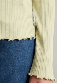 Lichtgroene geribde top met een scalloped zoom en lange mouwen, gecombineerd met donkerblauwe denim. Label leest "Marc O'Polo Denim."
