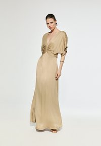 Long, flowing satin dress in a soft beige tone. Features a deep V-neck and gathered front detailing. Smooth texture with a slight sheen.