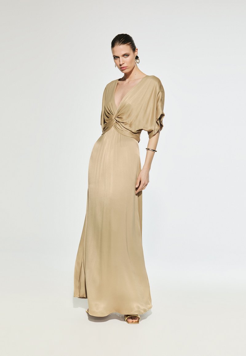 Long, flowing satin dress in a soft beige tone. Features a deep V-neck and gathered front detailing. Smooth texture with a slight sheen.