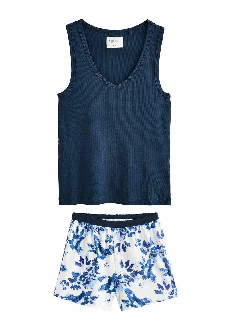 Cămașă fără mâneci, de culoare albastru închis, cu guler în V, asociată cu pantaloni scurți albi cu un model floral albastru și o talie elastică.