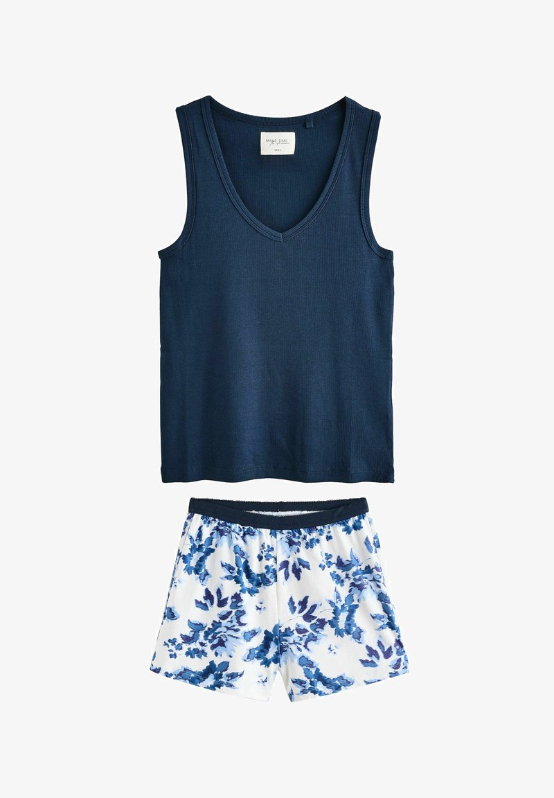 Cămașă fără mâneci, de culoare albastru închis, cu guler în V, asociată cu pantaloni scurți albi cu un model floral albastru și o talie elastică.