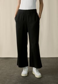 Schwarze, weit geschnittene Hosen mit einem elastischen Bund und seitlichen Taschen, aus einem glatten Stoff gefertigt. Kombiniert mit weißen Sneakern.