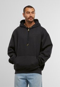 Schwarzer Hoodie mit Kordelzug und goldenen Akzenten, ausgestattet mit einer Fronttasche und gesticktem Logo. Weicher Stoff mit lockerem Schnitt.