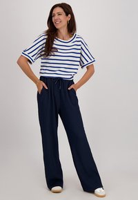 Witte gestreepte top met blauwe strepen, gecombineerd met marineblauwe broek met wijde pijpen, een textuurafwerking en een koord in de taille. Witte sneakers.