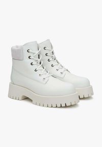 Witte veterschoenen tot de enkel, gemaakt van leer met een gestructureerde suede kraag, chunky witte zool en metalen oogjes voor de veters.