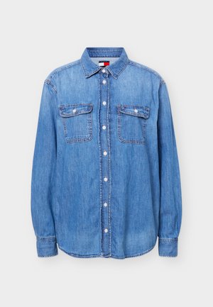 Chemise en denim bleu clair boutonnée à manches longues, avec deux poches à rabat à l'avant et un col, présentée sur un fond blanc.