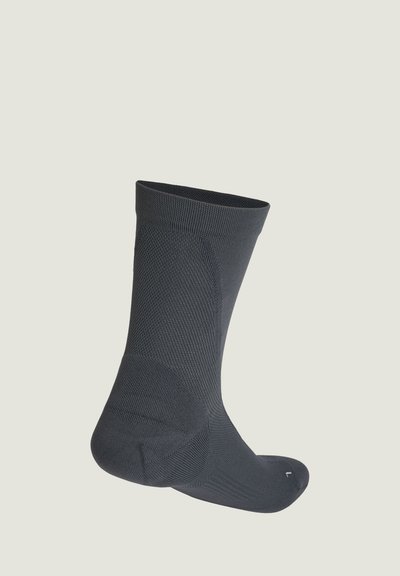 Schwarze knöchellange Socke mit strukturiertem Strickmuster, aufrecht vor hellem Hintergrund gezeigt.