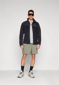 Musta fliisjakk, all valge hall t-särk, oliivrohelised cargo-pikkpüksid, mustad sokid ja hallide detailidega tossud.