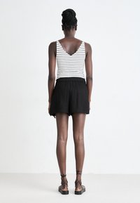Shorts noirs en lin associés à un débardeur rayé avec un décolleté en V et une coupe décontractée, complétés par des sandales à lanières.