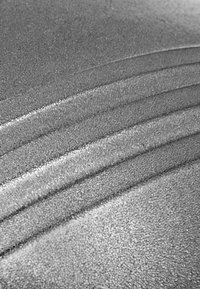 Texturierte Oberfläche mit glatten, geschwungenen Linien. Grau mit einer glänzenden, reflektierenden Qualität und kleinen, einheitlichen Blasen oder Perlen auf dem Material.