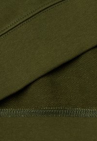 Tela verde oliva con una textura suave, que cuenta con una costura en la parte superior y una sección acanalada. La costura es visible a lo largo del borde.