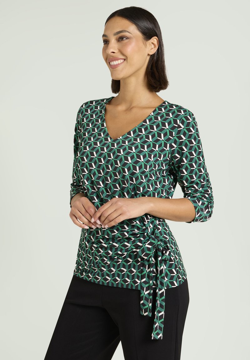 Groen zwart top met patroon, V-hals, driekwart mouwen en een strikdetail aan de zijkant. Heeft geometrische vormen in wit en lichte groene accenten.