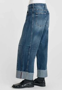 Jeans di denim ampi con un lavaggio azzurro chiaro, caratterizzati da un orlo risvoltato e quattro tasche. Texture liscia con leggera scoloritura e cuciture a contrasto.
