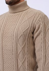 Pull en maille beige à col roulé présentant des motifs en câble texturé et des designs en diamants, fabriqué dans un tissu doux et chaud.