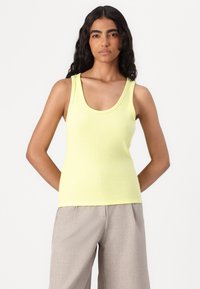 Limegul ribbet tanktopp med rund hals, tettsittende design og tykke stropper, stylet med lysegrå bukser.