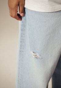 Lyseblå denimjeans med en flossede rift på venstre lår, der viser hvide tråde under. Glat tekstur med en afslappet pasform.