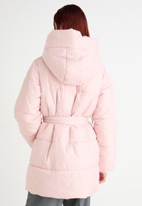 Rosa boblejakke med hette, belte i midjen og kviltet design. Har en myk, glatt tekstur og en kne-lengde silhuett.
