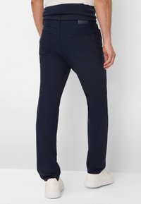 Pantalon bleu marine avec une ceinture texturée, en matière élastique, deux poches arrière et une coupe slim, associé à des baskets blanches.