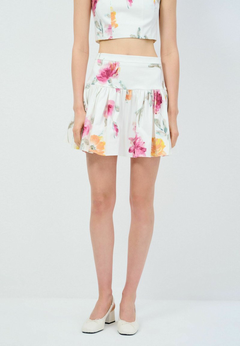 Weißer Rock mit floralem Druck und Rüschen, verziert mit rosa und orangefarbenen Blumen. Hergestellt aus leichtem Stoff, mit einer taillierten Silhouette gestaltet.