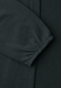 Manchon en tissu vert foncé avec détail de bord-côte élastique froncé, montrant la texture tricotée et les lignes de couture.