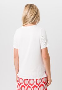Witte t-shirt met korte mouwen en een ronde halslijn, voorzien van zijsplitten, gemaakt van een zachte, lichte stof, gedragen met een rode rok met een patroon.