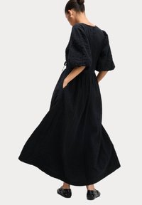 Schwarzes Maxikleid mit Puffärmeln, strukturiertem Stoff und seitlichen Taschen. Verfügt über eine lockere Passform und einen taillierten Schnitt für einen bequemen Bewegungsablauf.