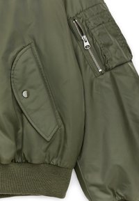Olivengrøn jakkeærme med en lynlåslomme, lomme med klap og trykknap samt ribbet manchet.
