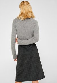 Pull en tricot gris à manches longues avec une jupe noire à carreaux ajustée comportant des accents bleu clair. Vue arrière, fond uni.