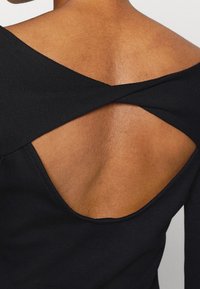 Top nero a coste con un design asimmetrico, caratterizzato da spalline incrociate sulla schiena e una schiena scoperta, che mette in risalto la texture della pelle.