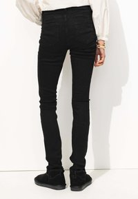 Jeans skinny noirs en denim, dotés d'une taille haute, de deux poches arrière et d'une coupe ajustée jusqu'aux chevilles, associés  à des bottines.