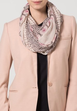 Personne portant une écharpe infinie rose à motifs sur un haut noir et un blazer rose clair avec un seul bouton fermé.