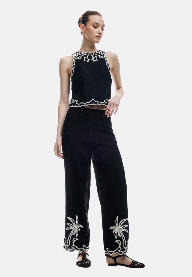 Svart tvådelat plagg bestående av en cropped topp med scallopade kanter och dekorativ broderi, i kombination med vida byxor prydda med palmträdsmotiv.
