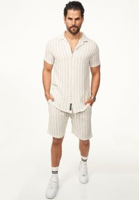 Cremfarbendes Kurzarmhemd und passende Shorts mit vertikalen Streifen. Weicher Stoff, leichtes Material und lässige Passform. Weiße Sneaker runden den Look ab.