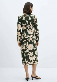 Haljina dugih rukava s cvjetnim uzorkom u tamnozelenoj boji, s svijetlopinkim cvjetovima, koji ima strukiranu liniju i ravni siluetu.