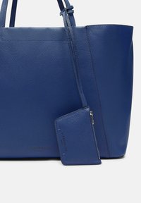 Sac fourre-tout en cuir bleu avec une finition texturée, comprenant un porte-cartes amovible et des poignées doubles pour un transport facile.