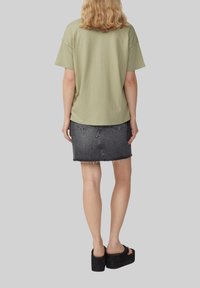 T-shirt en coton vert olive à manches courtes, associé à une jupe en jean noir déchiré et des sandales à plateforme noires.