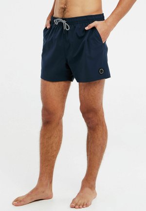 Marineblaue Badeshorts mit einem elastischen Bund, Kordelzug und seitlichen Taschen. Mit einem runden Logo am linken Bein. Glatter Textur.